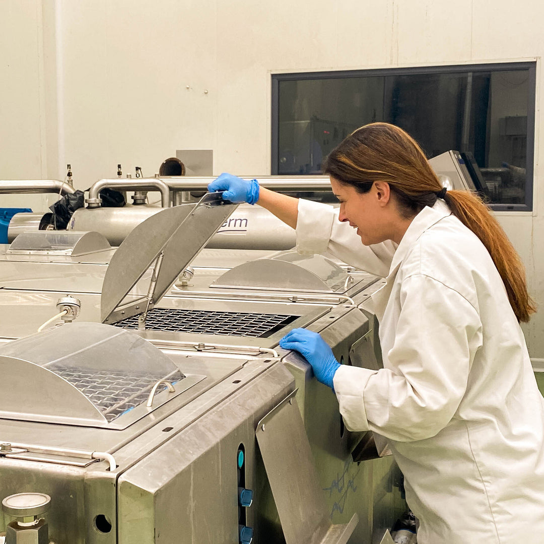 Person in a lab coat and gloves working with equipment in an olive oil mill